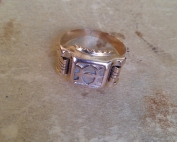 טבעת חותמת ישנה מקורית עם אות מרכזית ועיטורים בצדדים על משטח בהיר