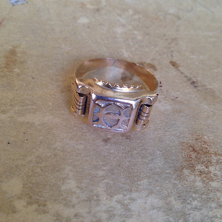 טבעת חותמת ישנה מקורית עם אות מרכזית ועיטורים בצדדים על משטח בהיר